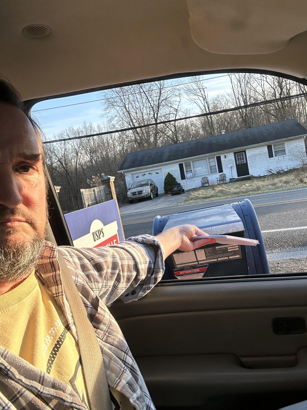 An agent dropping a stack of sealed cards into a mailbox from his car